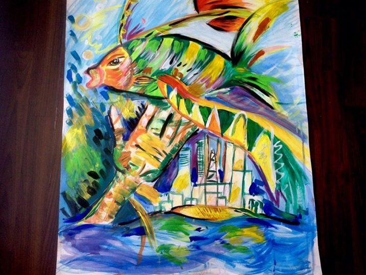 Malba na papíře - veliká ryba, pod kterou je natažená ruka, přelétává nad městem. V pozadí svítí veliké slunce.